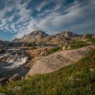 Image: Water rushing from rocky terrain into a lake, surrounded by wildflowers. Above Island Lake photo credit Scott Copeland.
