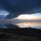 Image: a photo of a body of water with industrial stacks emitting large plumes of pollution.