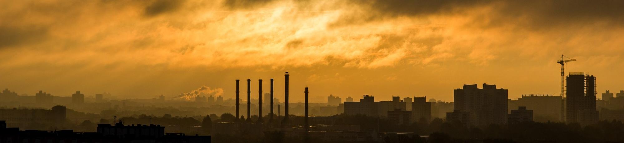 Image: a industrial emissions envelope a metropolitan area at dusk. Image by Free-Image of Pixabay. End ID.